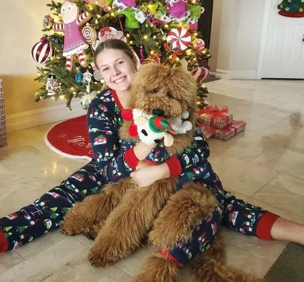 A girl in pajamas sitting on the floor with her dog.